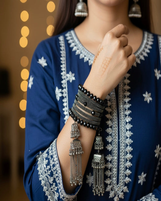 Person wearing a blue embroidered outfit with silver jewelry, including bangles and earrings.