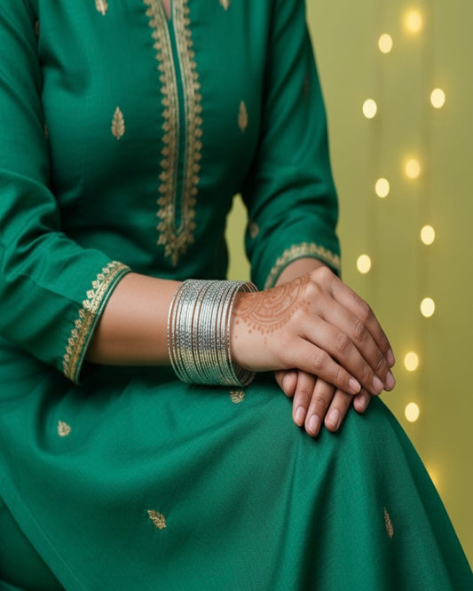 Green traditional outfit with gold embroidery and silver bangles on a blurred background